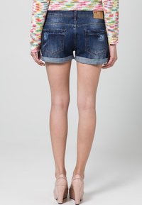 Shorts de denim con un lavado azul oscuro, dobladillo enrollado, detalles desgastados en los bolsillos traseros y un parche de cuero marrón en la cinturilla.