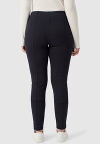 Granatowe legginsy wykonane z elastycznego materiału, z wysokim stanem i efektywnym detalem szwów, w połączeniu z białymi sneakersami.