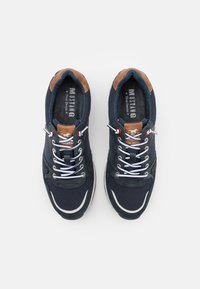 Marinblå sportskor med meshöverdel, bruna mockadetaljer, vita snören och gummisula. Har logotyp på tungan och sidan.