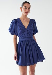 Mornarsko modra obleka s napihnjenimi rukavi, globokim V-izrezom, nabranim zgornjim delom in slojevito krilo. Ima čipkast rob ob robu in pasu.