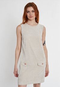 Beiges Corduroy-Ärmelloses Kleid mit Rundhalsausschnitt, zwei Vordertaschen und Holzknopf-Akzenten. Strukturierter Stoff mit vertikalen Linien.