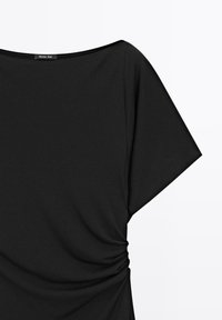 Schwarzes Oberteil mit einem Boot-Ausschnitt, breiten, kurzen Ärmeln und Raffung an den Seiten. Hergestellt aus weichem Stoff mit glatter Textur.