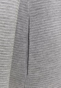 Grå ribbat tyg med en vertikal struktur. Har en sidoklyvning som förbättrar flexibilitet och rörelse i designen. Inga ytterligare dekorationer synliga.