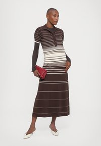 Rochie polo tricotată, cu dungi orizontale maro și crem, guler cu nasturi și o siluetă evazată; asortată cu o poșetă roșie și încălțăminte albă.