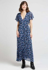 Robe fluide fleurie bleu marine avec des motifs bleus et jaunes, décolleté en V, manches courtes volantées et jupe fluide, associée à des bottes à talons noires.