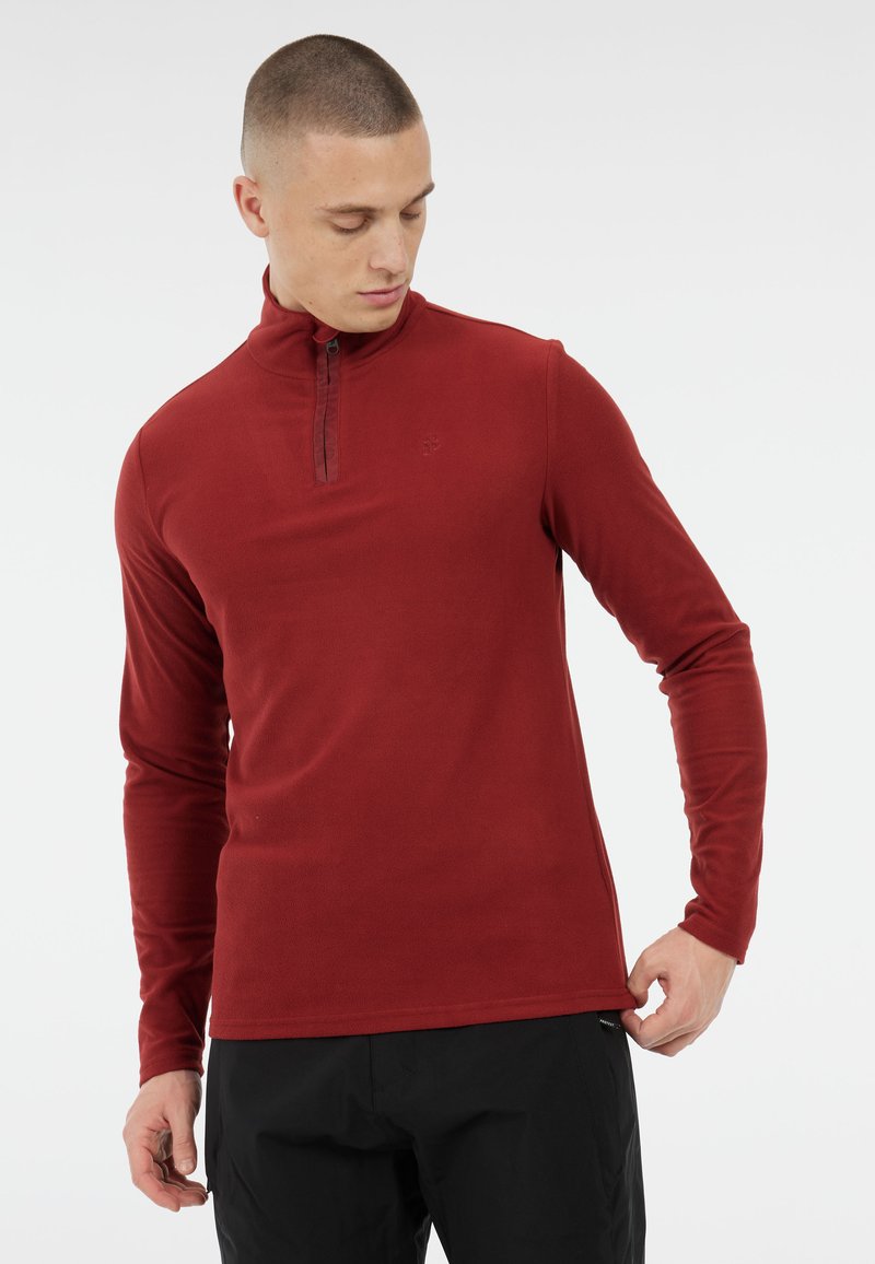 Pullover in pile rosso con colletto zip a metà e maniche lunghe; presenta una texture liscia e un design aderente con dettaglio del logo sul petto.