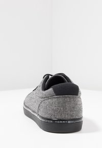 Sneaker in tessuto grigio con accenti neri, caratterizzato da una finitura liscia, forma arrotondata e suola in gomma con il logo di Tommy Hilfiger.