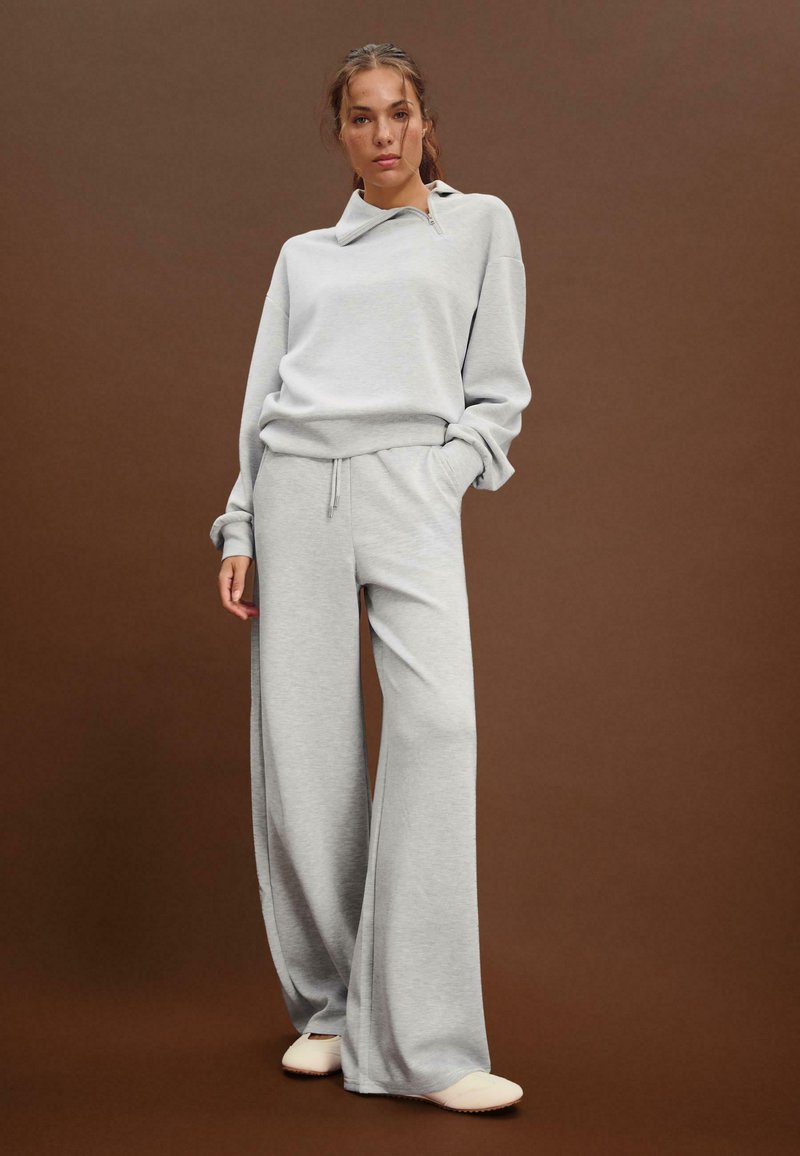Lysegrå oversized sweatshirts med høj krave, parret med grå bukser med brede ben. Blød tekstur, afslappet design, minimal hardware.