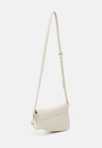 Lille cremefarvet crossbody taske med justerbar rem og subtilt guldfarvet hardware, præsenteret mod en simpel hvid baggrund.