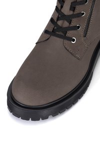 Gai pelēki sintētiski potītes zābaki ar melnām šņorēm, sudraba acs caurumiem un strukturētu gumijas zoli. Aprīkoti ar sānu rāvējslēdzēju, kas nodrošina ērtu piekļuvi.