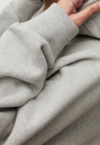 Felpa con cappuccio grigio chiaro realizzata in tessuto morbido e dalla texture marcata con vestibilità comoda. Presenta una grande scollatura con cappuccio e polsini a coste.