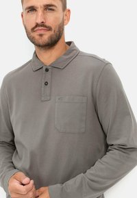 Grijze lange mouwen polo met een collerende halslijn, drie-knopen sluiting en borstzak aan de linkerkant. Soepele katoenmateriaal met een relaxte pasvorm.