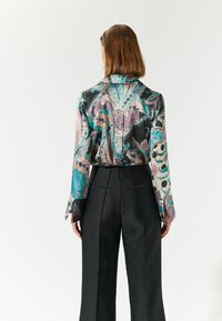 Blusa di seta con un motivo floreale colorato, presenta maniche lunghe e un colletto sartoriale, abbinata a pantaloni neri a vita alta.