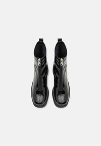Botine din piele lăcuită negre, cu fermoar frontal, vârf rotund și panouri laterale texturate. Talpă din cauciuc plat și buclă de prindere la călcâi.