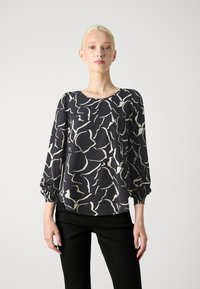 Blusa a righe bianche e nere con maniche lunghe a sbuffo e scollatura rotonda, realizzata in tessuto liscio e con polsini arricciati.