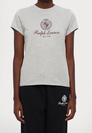 Osoba nosząca jasnoszarą koszulkę Ralph Lauren z herbem oraz czarne spodnie z tym samym logo na górnej części uda.