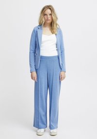 Completo blu chiaro composto da giacca attillata e pantaloni a gamba larga, realizzato in tessuto morbido, abbinato a scarpe bianche. Design semplice.