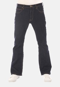 Donkerblauwe spijkerbroek met een rechte pijp, subtiele stikseldetails, vijf zakken en een ritssluiting aan de voorkant. Gecombineerd met witte sneakers.