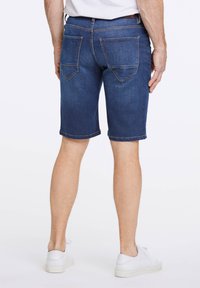 Pantalones cortos de mezclilla azul oscuro con cinco bolsillos, costuras en contraste y puños doblados, combinados con zapatillas blancas.