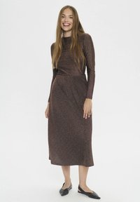 Braunes, langärmliges Kleid aus schimmerndem Strick mit taillierter Passform und Midi-Länge. Glatte Textur, dezentes metallisches Muster, kombiniert mit schwarzen Ballerinas.