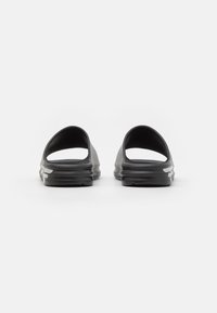 Svarta slip-in sandaler med en slät gummitextur, öppen bakdel och en formad design. Har vita logotypdetaljer på sidan.