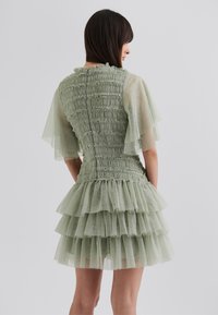 Tulle dress in pale green; sheer flutter sleeves, smocked bodice, and layered ruffle skirt create a textured, flowing design.