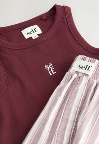Bordowy, prążkowany top na ramiączkach z białym logo "self.", połączony ze spodniami w jasnoróżowe i białe paski z dopasowaną metką. Miękki, casualowy materiał.