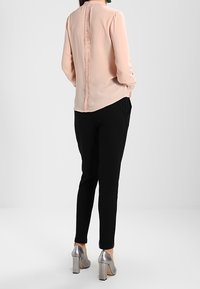 Peach long-sleeve blouse with a textured back, paired with black tapered pants and silver block-heeled shoes. Smooth fabric, minimalist design.