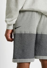 Nike-shorts med ett rutmönster på framsidan och en strukturerad mörkgrå nedre del, med uppvikta fållar och subtil branding.