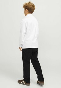 Vit långärmad skjorta med hög krage, kombinerad med svarta manchesterbyxor och bruna sneakers med vita detaljer.