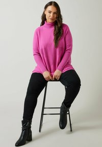 Maglione a maglia rosa con colletto alto, caratterizzato da un motivo a stelle e una texture a coste. Abbinato a jeans neri e stivali neri al ginocchio.