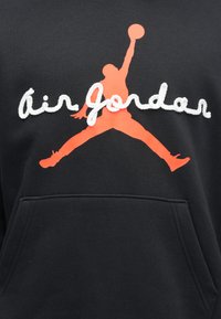 Μαύρο φούτερ με κουκούλα που διαθέτει μεγάλο πορτοκαλί λογότυπο "Jumpman" και λευκό κείμενο "Air Jordan", με τσέπη καγκουρό. Μαλακή υφή υφάσματος.