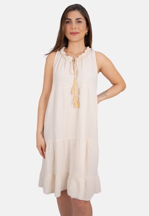 Weißes, gestuftes Kleid aus leichtem Stoff mit rüschenbesetztem Ausschnitt und Bindegürtel. Die Textur ist knitterig und weich, ideal für warmes Wetter.