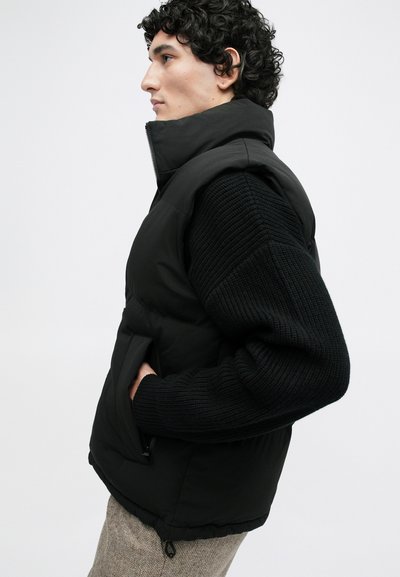 Zwarte gewatteerde vest met hoge kraag, voorzien van een textuur gebreide mouw, zijzakken en een trekkoord onderaan. Glad afwerking en modern ontwerp.