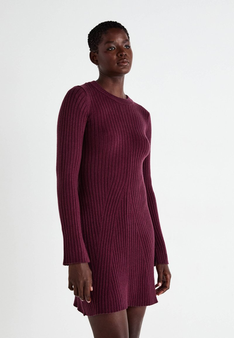 Abito in maglia a coste di un dark burgundy con maniche lunghe, scollatura a girocollo e spacchi laterali. Presenta linee verticali testurizzate su tutta la stoffa.