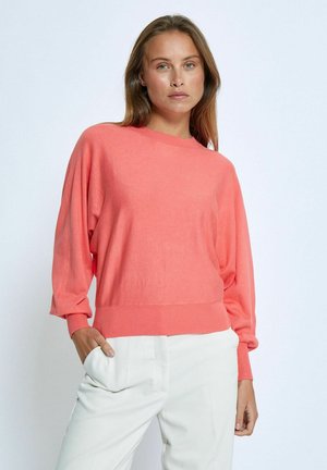 Coral pullover sweater with a round neckline, loose sleeves, ribbed cuffs and hem, made of soft knit material, paired with light trousers.