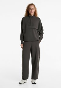 Dunkelgraues Sportset bestehend aus einem Pullover mit halbem Reißverschluss und hohem Kragen sowie weit geschnittenen Sweatpants. Hergestellt aus weichem, strukturiertem Material.