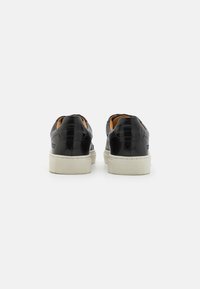 Czarne skórzane sneakersy o gładkiej fakturze, niskoprofilowym designie, białej gumowej podeszwie i subtelnym logo na pięcie.