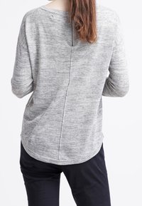 Lichtgrijs gebreid topje met een afgeronde zoom, voorzien van een middennaad en een ritsdetail aan de achterkant. Lange mouwen, losse pasvorm en zachte textuur.