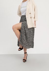 Svartvit mönstrad kjol med en hög slits, kombinerad med en vit t-shirt och beige kavaj. Utrustad med svarta högklackade sandaler.