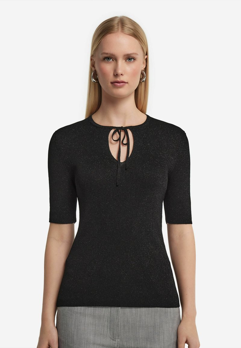 Svart stickad topp med korta ärmar, med rund ringning och en nyckelhålsöppning knuten med en svart dragsnodd. Subtil glittrande struktur.