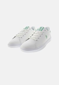 Białe sneakersy wykonane z gładkiego materiału syntetycznego, z zielonymi akcentami na języku i logo, z płaską białą gumową podeszwą.