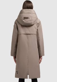 Dlhý béžový kabát s vysokým golierom a veľkou kapucňou. Výrazné prešívanie a logo nášivka na chrbte. Hladký, matný povrch.