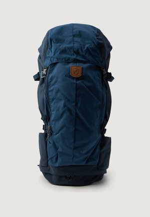 Navy blue backpack with a softshell design, adjustable top, leather logo patch, side pockets, and zippers for storage and access.