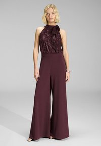 Jumpsuit borgogna con top a scollo all'americana in paillettes, dettaglio del nodo a fiocco sul collo e pantaloni a gamba larga. Tessuto morbido con vestibilità rilassata.