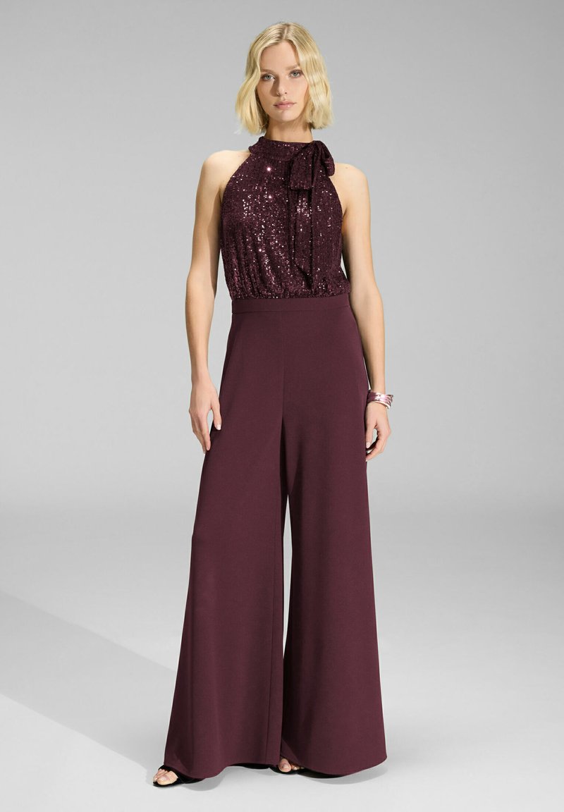 Jumpsuit borgogna con top a scollo all'americana in paillettes, dettaglio del nodo a fiocco sul collo e pantaloni a gamba larga. Tessuto morbido con vestibilità rilassata.