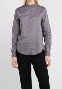 Camisa gris de manga larga con cuello subido, cierre delantero con botones y puños abotonados. Fabricada con una tela suave de textura sutil.