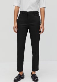 Zwarte op maat gemaakte broeken met een slim fit, vlakke voorkant, riemlussen en zijzakken. Gecombineerd met zwarte instappers en een wit t-shirt.