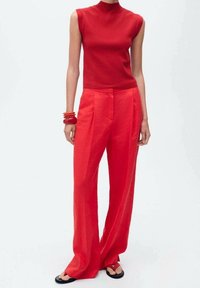 Haut rouge sans manches et pantalon rouge à jambes larges, tous deux en tissu lisse. Les accessoires comprennent des bracelets rigides rouges. Les chaussures sont des sandales noires.