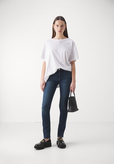 Fehér, oversized póló, sötét skinny farmerekkel, fekete lóferek arany hardware-rel, kis fekete kézitáska. Sima anyag, laza szabás, minimalista dizájn.